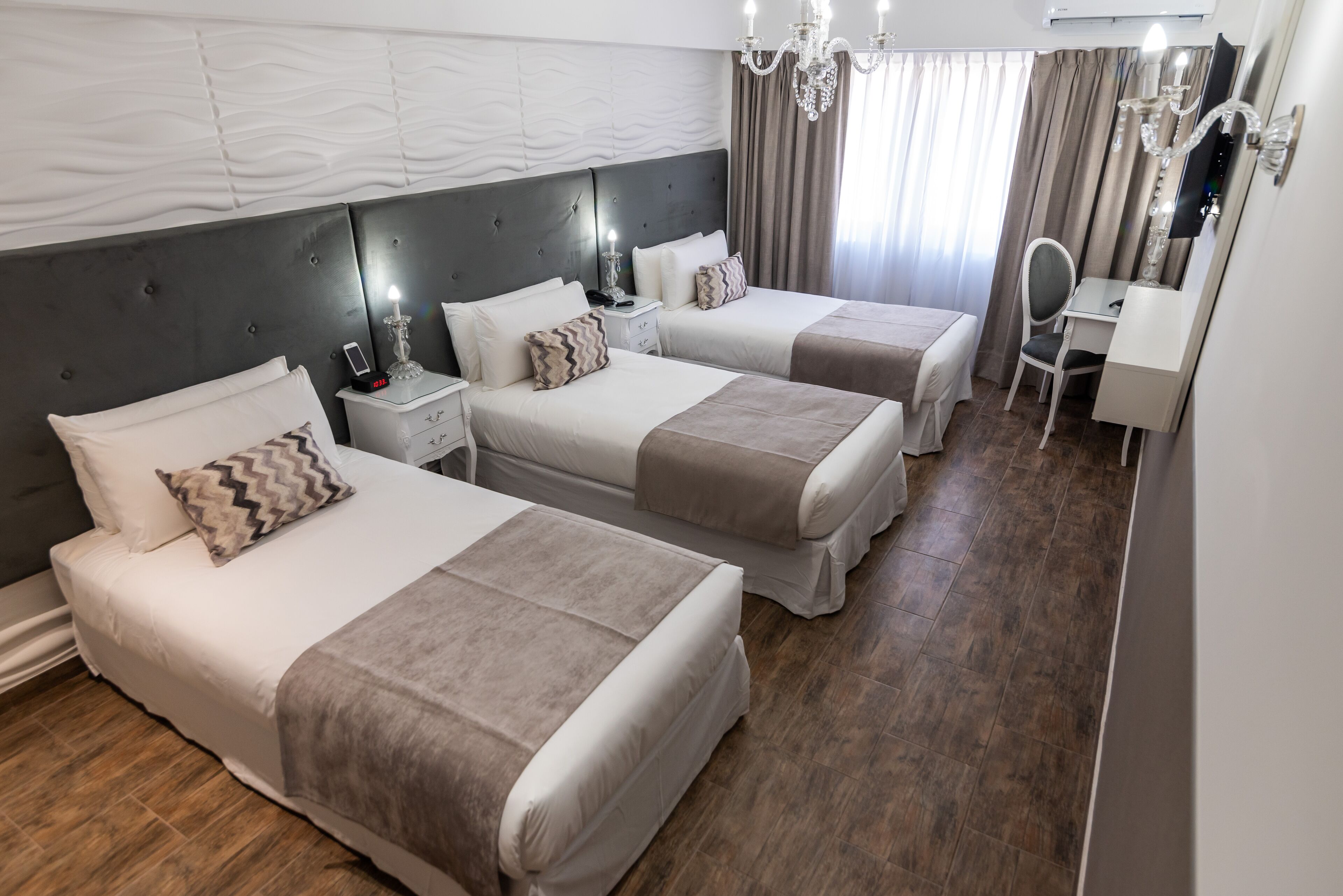 A hotel room with two beds, a desk, a chair, a vanity with a mirror, and a chandelier.