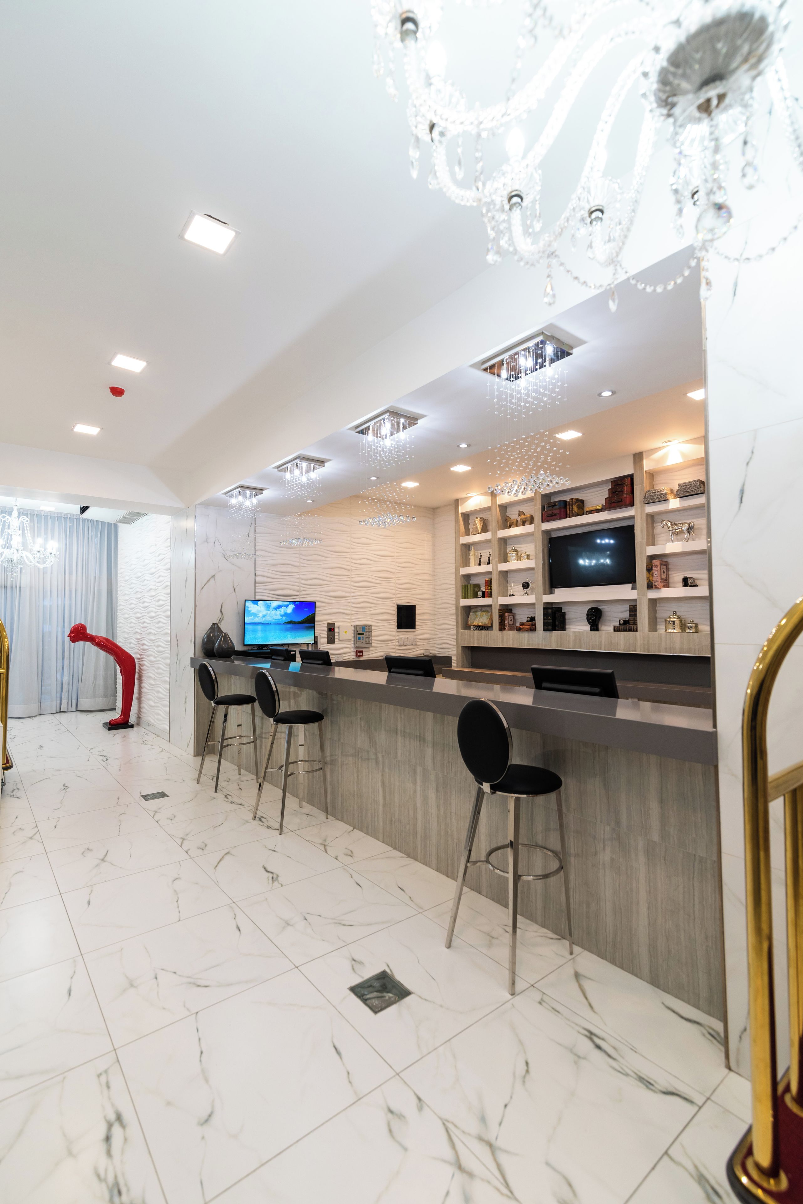 A modern bar area with marble flooring, bar stools, a television, and decorative lighting.