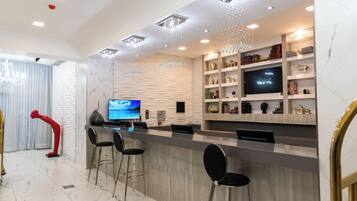 A modern bar area with marble flooring, bar stools, a television, and decorative lighting.