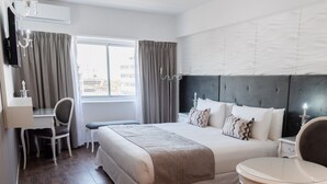 Una habitación de hotel con una cama grande, un escritorio, una silla, una mesa redonda y una ventana con cortinas.