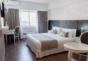 Una habitación de hotel con una cama grande, un escritorio, una silla, una mesa redonda y una ventana con cortinas.