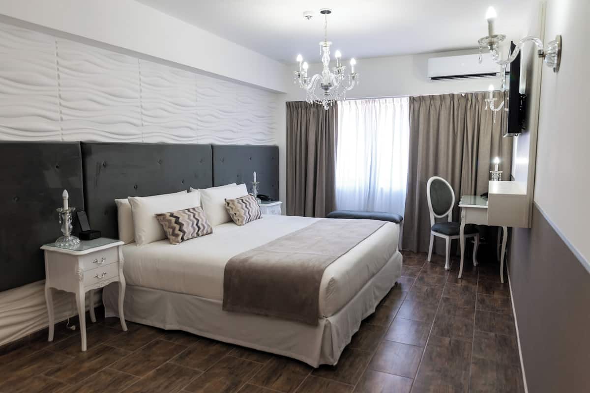 A modern hotel room with a large bed, bedside table, and a desk with a chair.
