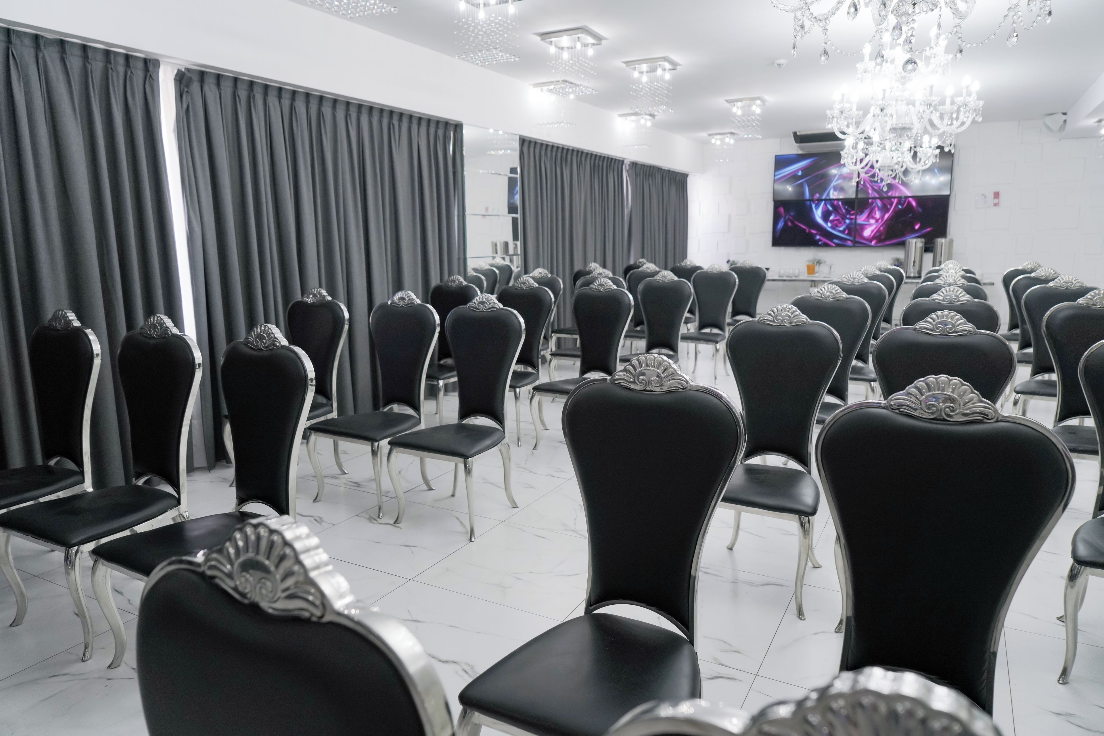 Un salón de conferencias con filas de sillas negras, una araña de cristal y un televisor de pantalla plana en la pared.