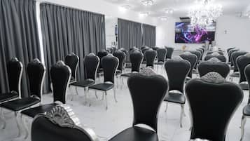 Un salón de conferencias con filas de sillas negras, una araña de cristal y un televisor de pantalla plana en la pared.