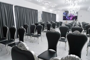 Un salón de conferencias con filas de sillas negras, una araña de cristal y un televisor de pantalla plana en la pared.