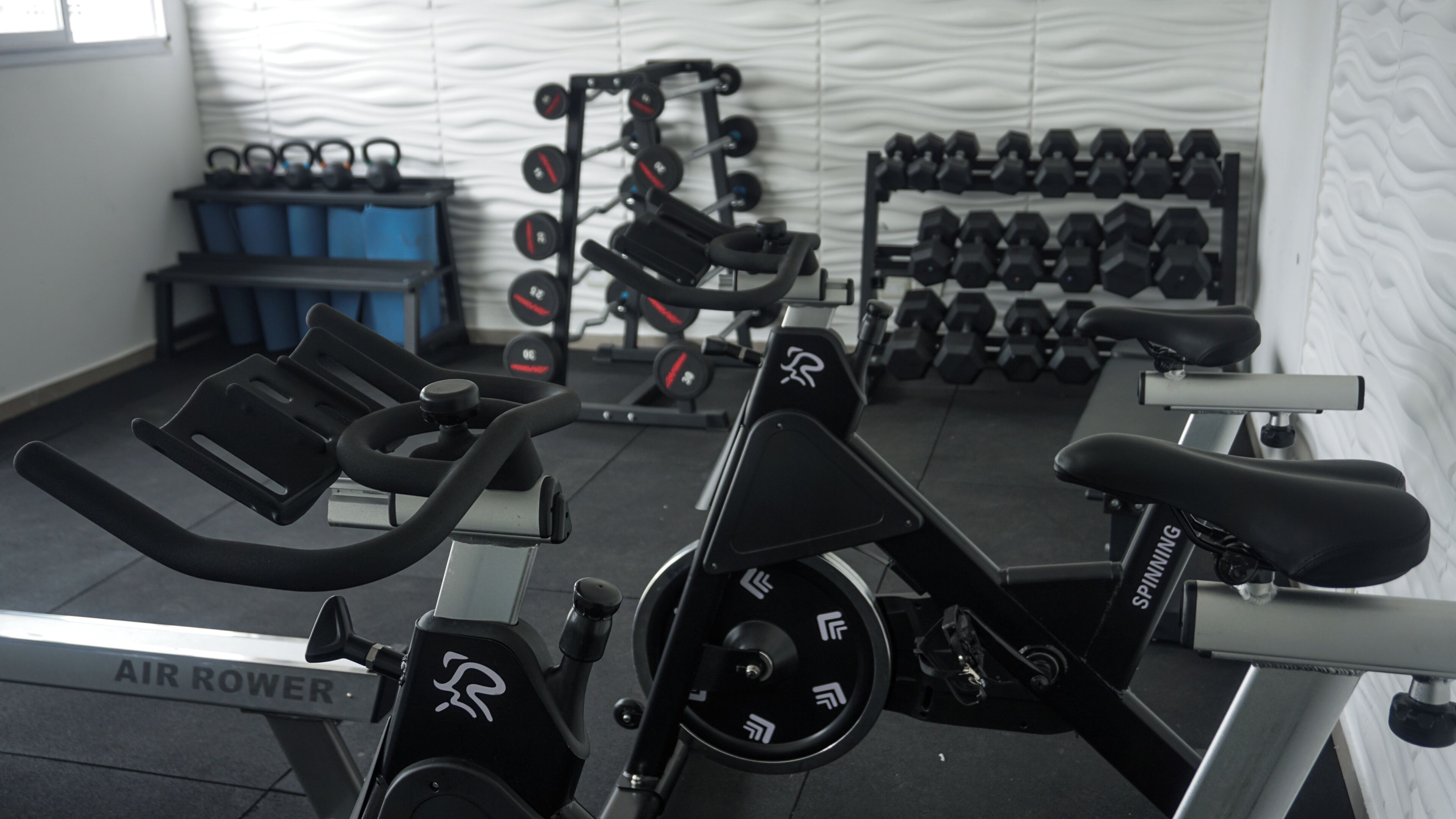 Una bicicleta estática, un soporte de mancuernas en la pared y un banco para pesas en un gimnasio.