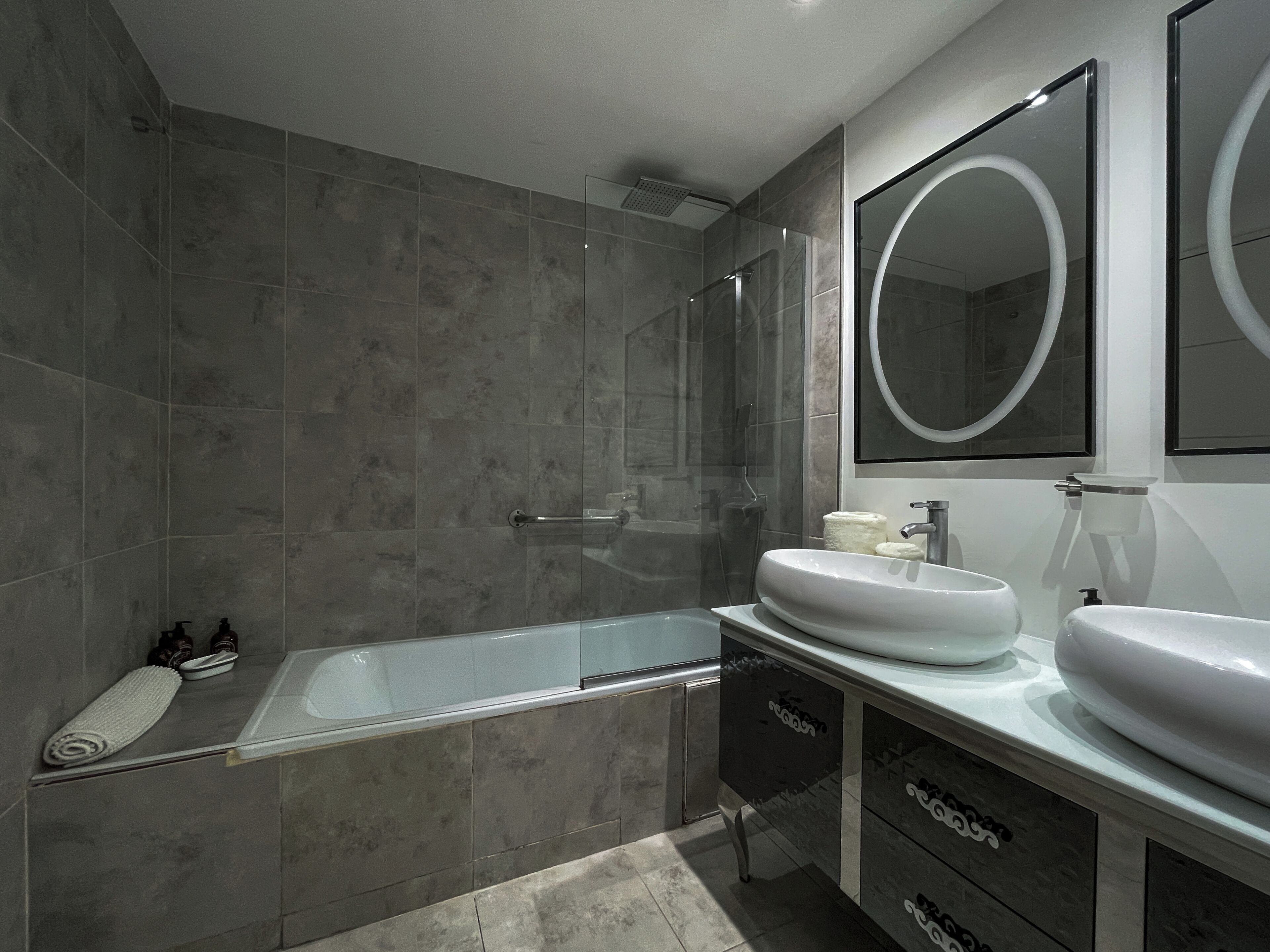 Un baño moderno con cabina de ducha de vidrio, un espejo grande y un tocador con dos lavabos.