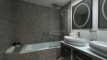 Un baño moderno con cabina de ducha de vidrio, un espejo grande y un tocador con dos lavabos.