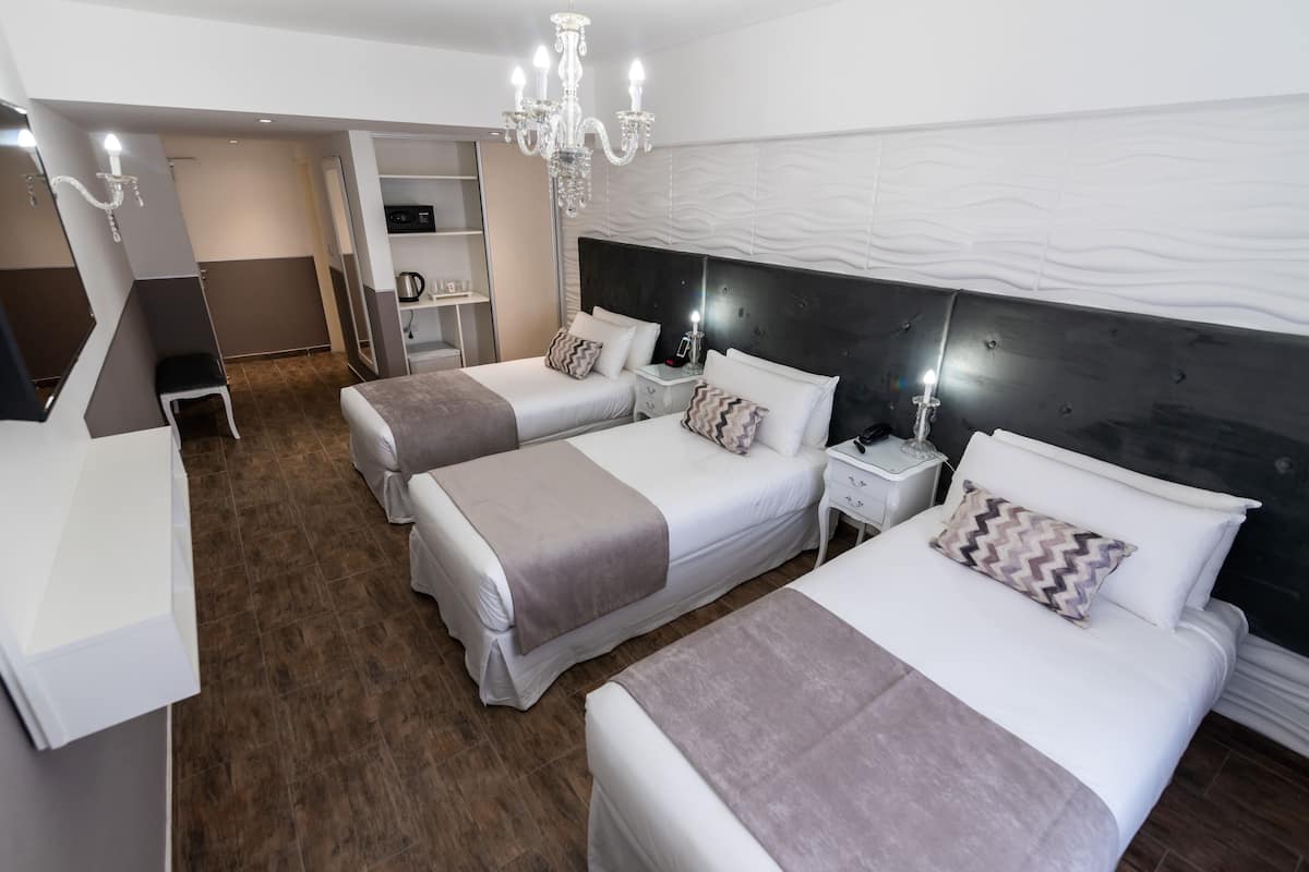 A hotel room with two beds, a chandelier, a wardrobe, and a desk.