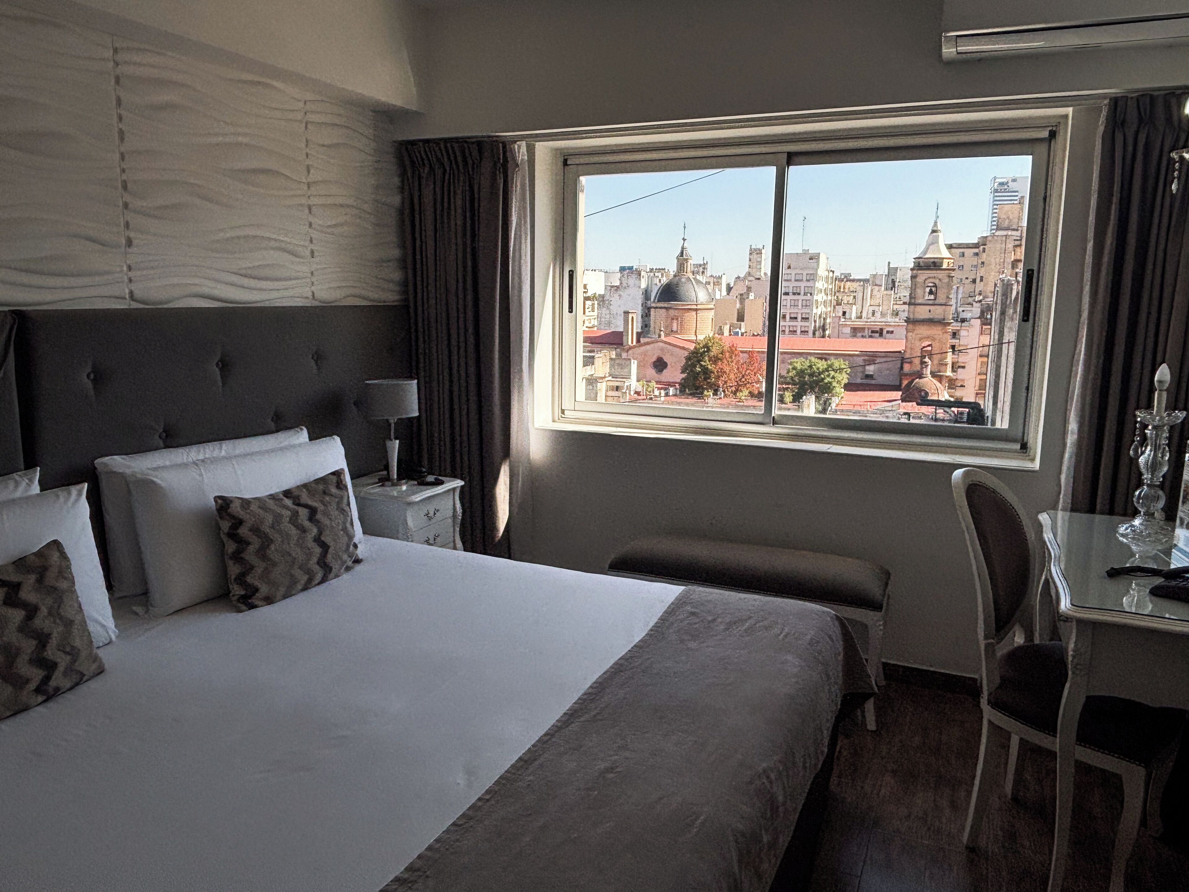 A hotel room with a large bed, a desk, and a view of the cityscape.