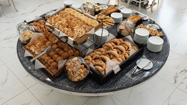 Una mesa de buffet con diversos productos horneados y pasteles, incluyendo croissants, muffins y galletas, dispuestas sobre una mesa de mármol en un comedor.