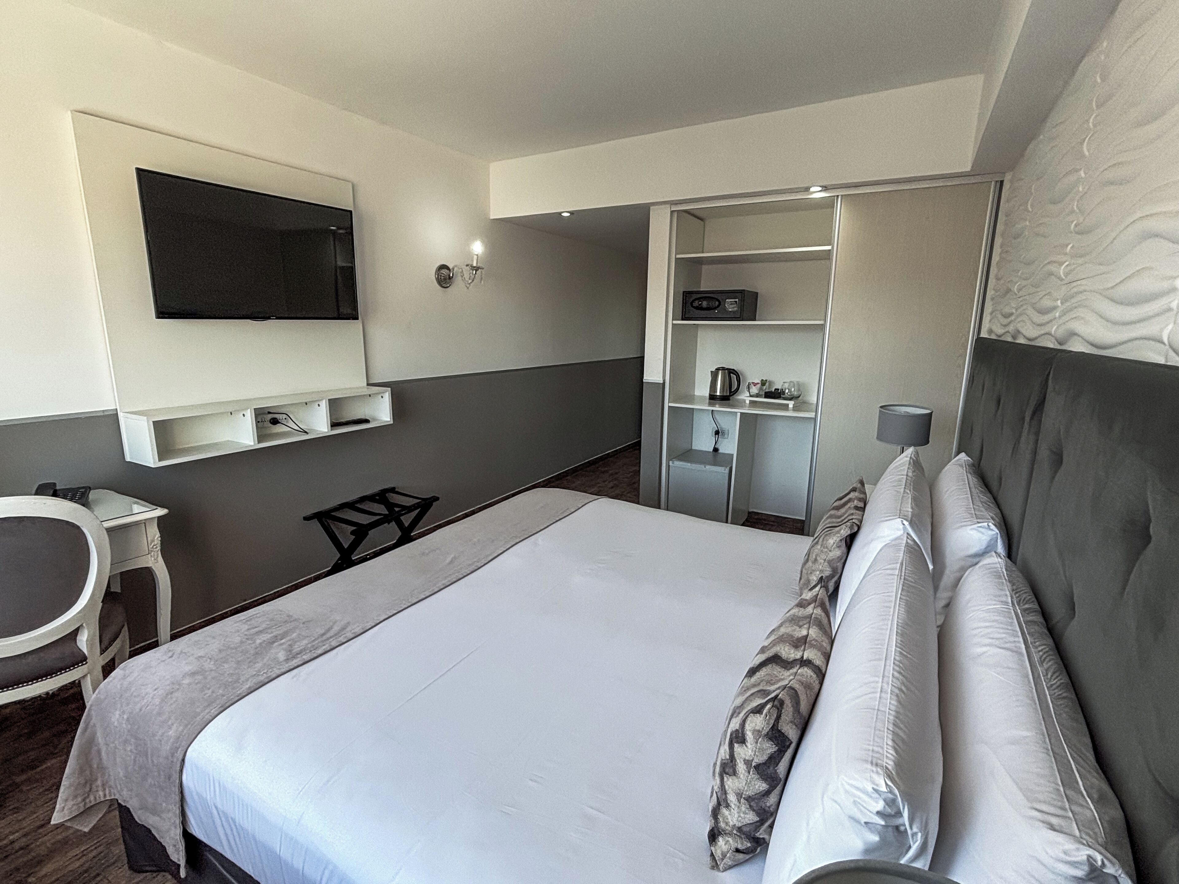 Habitación de hotel con una cama, televisión montada en la pared, escritorio y armario.