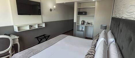 Habitación de hotel con una cama, televisión montada en la pared, escritorio y armario.