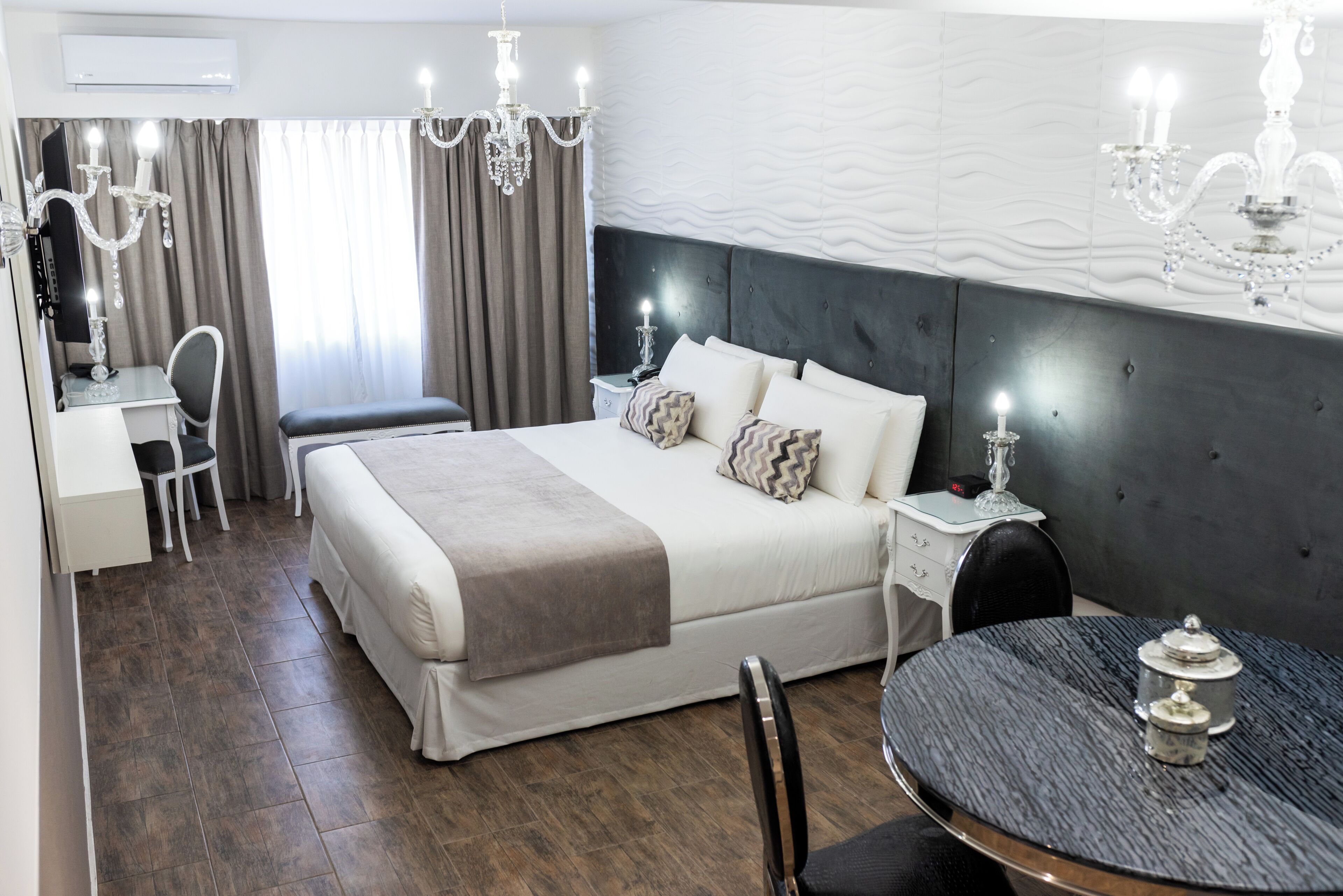 A hotel room with a bed, bedside table, lamp, chair, desk, and a round table with a lamp.