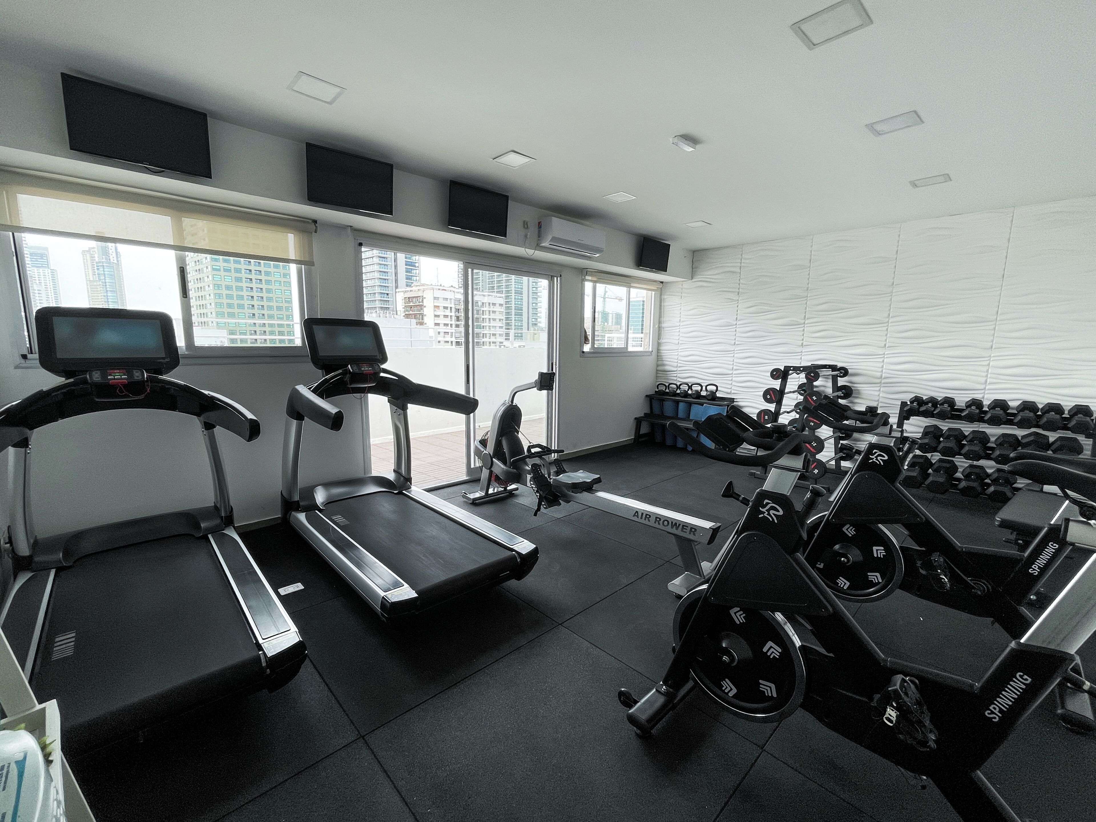 Un gimnasio con cintas de correr, bicicletas estáticas y pesas.