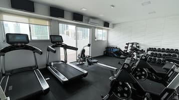 Un gimnasio con cintas de correr, bicicletas estáticas y pesas.