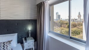 Habitación de hotel con cama, mesita de noche con lámpara y ventana con vista a la ciudad.