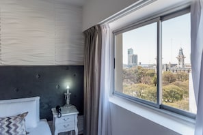 A hotel room with a bed, a bedside table with a lamp, and a window with a cityscape view. - Ker San Telmo Hotel (Buenos Aires)