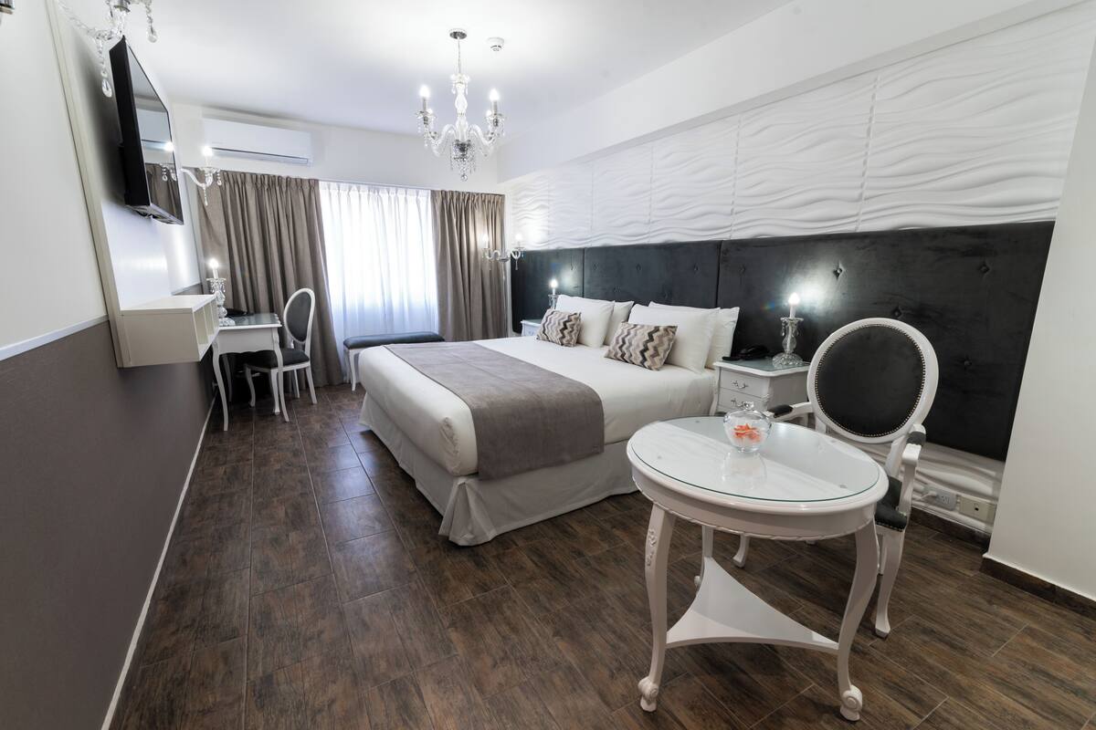 A modern hotel room with a large bed, a desk, a chair, a round table, and a mirror.