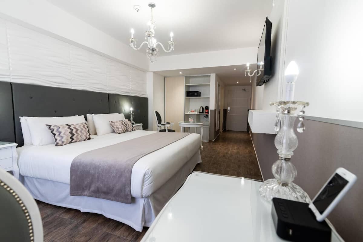 A hotel room with a bed, bedside table, TV, and a desk with a phone.