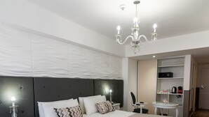 Habitación de hotel moderna con una cama grande, una mesita de noche con lámpara, una pequeña mesa con silla y un escritorio empotrado con silla.