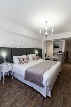 A modern hotel room with a large bed, a bedside table with a lamp, a small table with a chair, and a built-in desk with a chair. - Ker San Telmo Hotel (Buenos Aires)