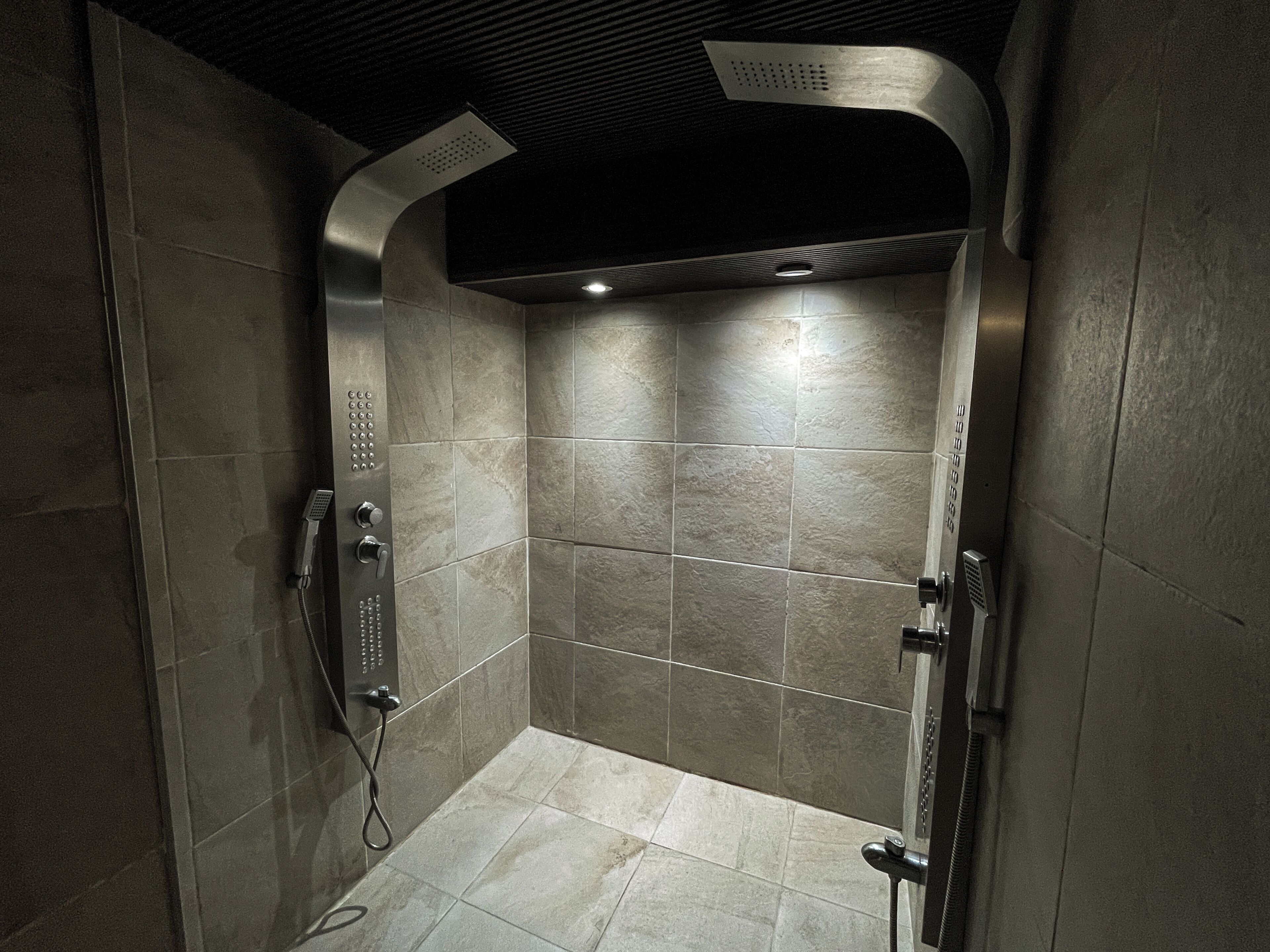 A modern shower stall with a curved showerhead, a handheld shower attachment, and a control panel.