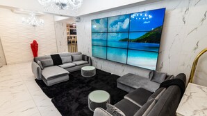 Una sala de estar moderna con un sofá modular, un tapete negro y un televisor grande mostrando un paisaje pintoresco.