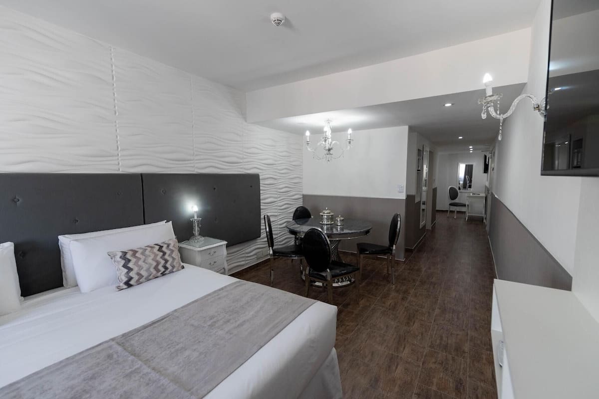 A hotel room with a large bed, a desk, a chair, and a chandelier.