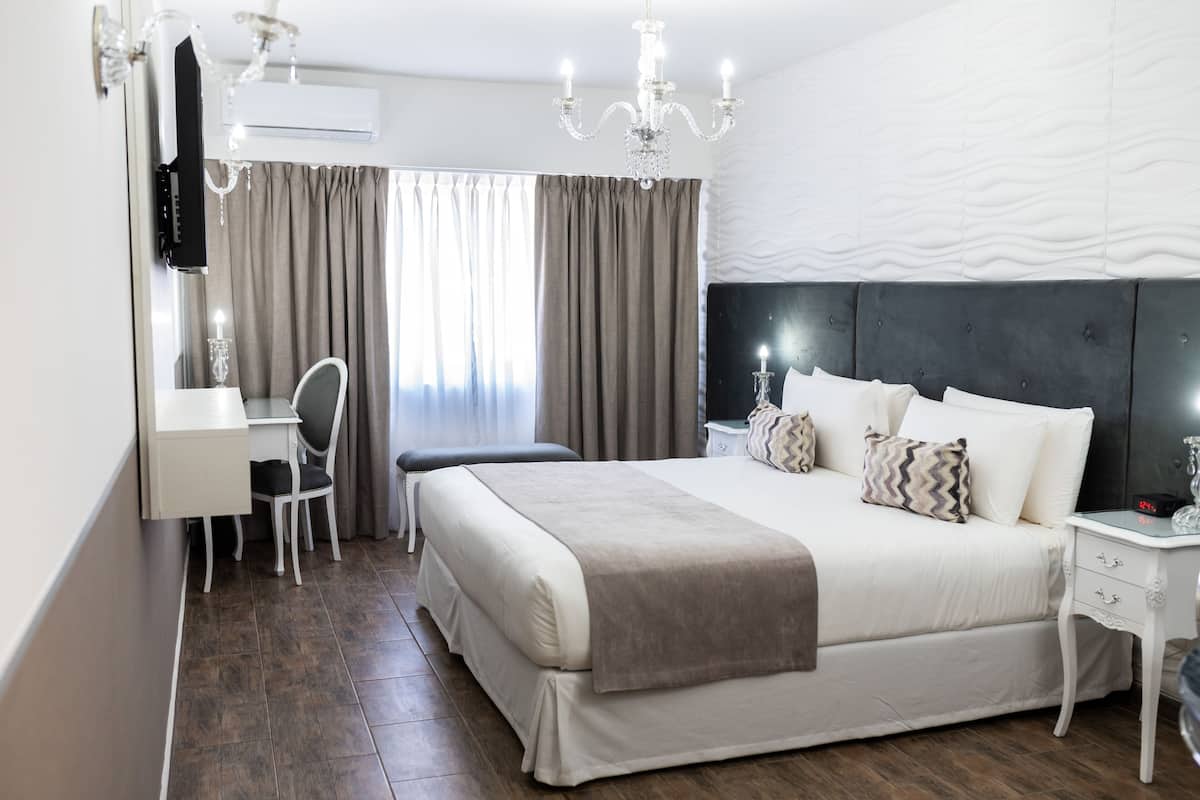 A bedroom with a bed, bedside table, lamp, and a desk with a chair.
