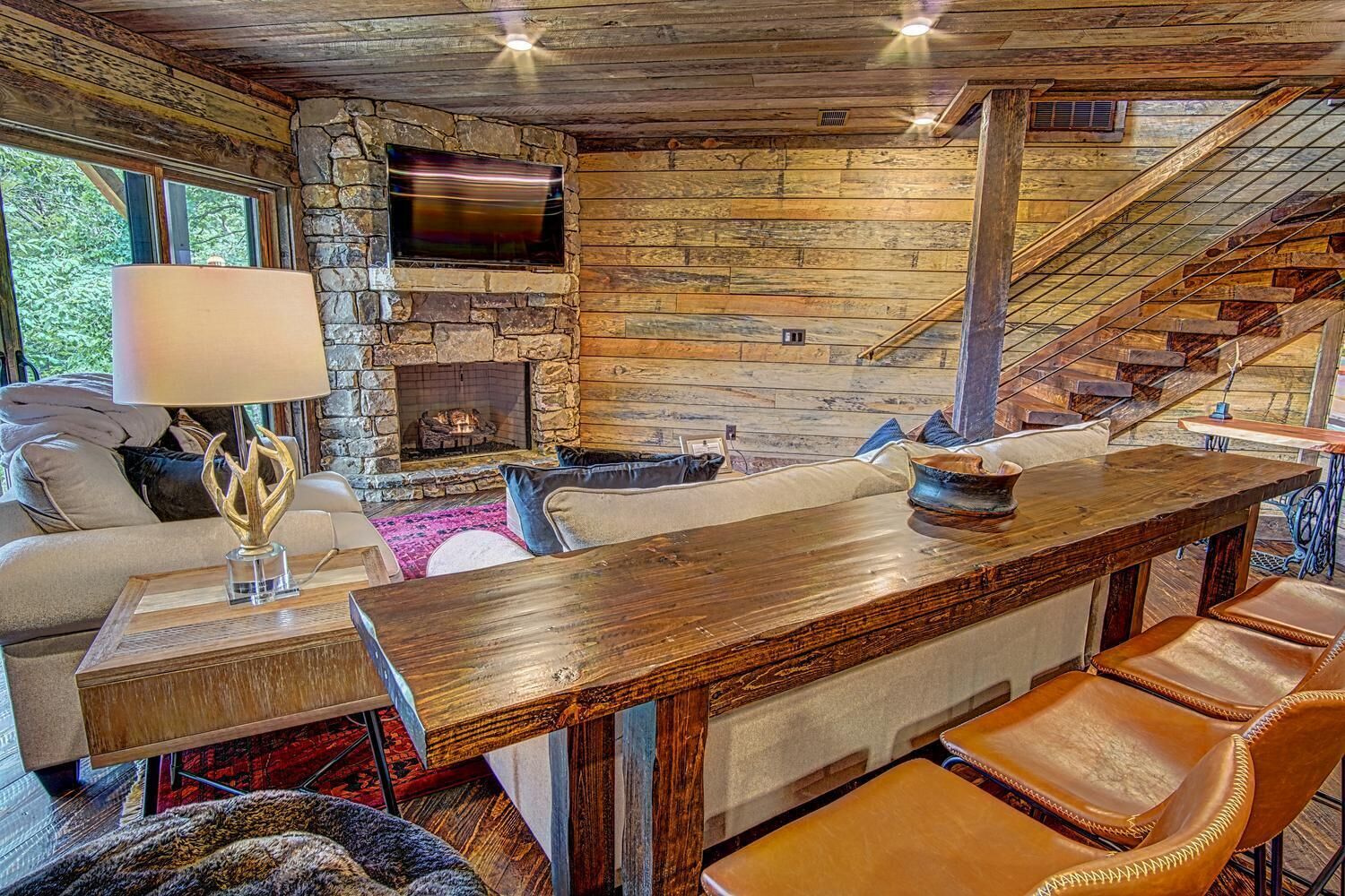 Un intérieur rustique avec une cheminée en pierre, des murs en bois, un canapé, une table basse et des fauteuils en cuir.