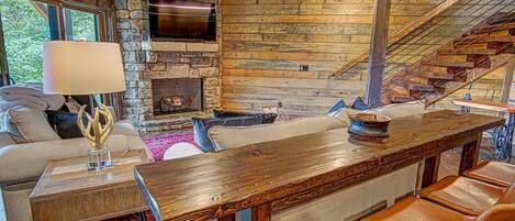 Un intérieur rustique avec une cheminée en pierre, des murs en bois, un canapé, une table basse et des fauteuils en cuir.