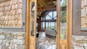 A wooden exterior with stone accents, a large glass door leading to a spacious interior with a stone floor and a view of the outdoors. - Luxury Cabin with amazing sunsets! Close to Downtown Blue Ridge! (Blue Ridge)
