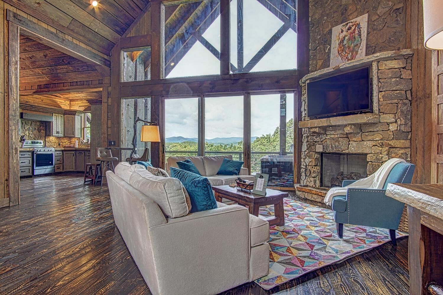 A spacious living room with a fireplace, large windows, and a kitchen in the background.
