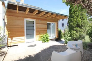 Ein Holzhaus mit einer Veranda, einem kleinen Garten und Sitzgelegenheiten im Freien.