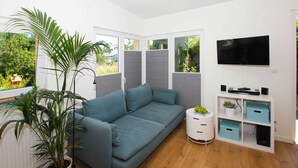 A modern living room with a grey sofa, a flat-screen TV, and a white storage unit with blue drawers. - 01: 34 m², 2-room, 2 pers., Terrace, WL - Villa Elise in Ostseebad Göhren (Göhren)