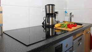 A modern kitchen with a black countertop, stainless steel coffee maker, and a cutting board with vegetables. - 01: 34 m², 2-room, 2 pers., Terrace, WL - Villa Elise in Ostseebad Göhren (Göhren)