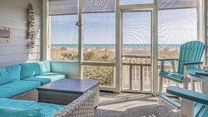 Une véranda avec une grande porte vitrée donnant sur la plage, un ventilateur de plafond et un canapé de couleur turquoise.