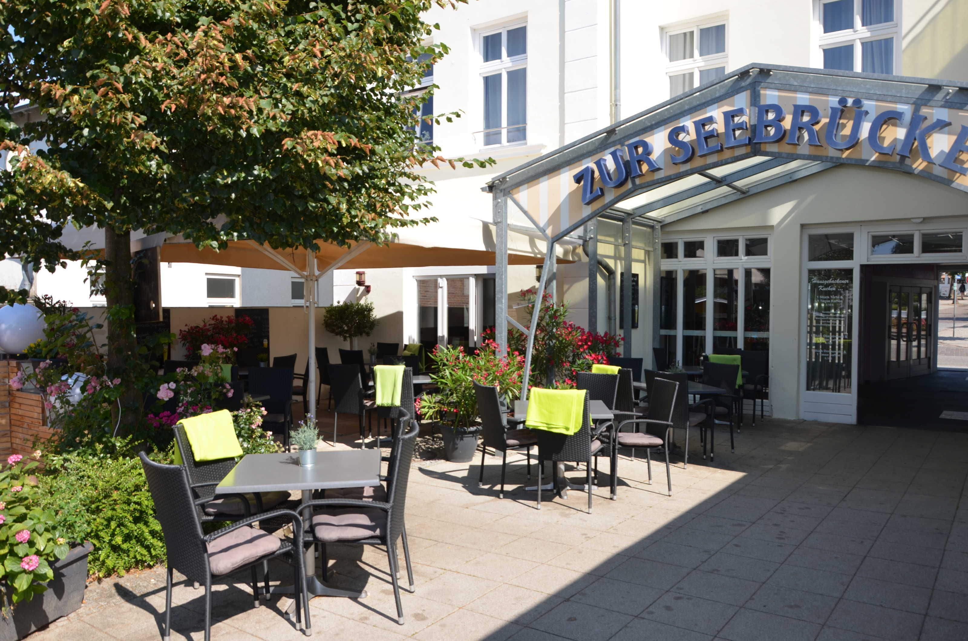 Een terras met tafels en stoelen, een overdekte ingang en plantenbakken.
