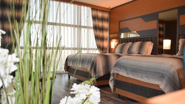 A hotel room with two beds, a large window with sheer curtains, a mirror, and a bedside table with a lamp. - Grand Rimedya Hotel Bursa (Bursa)