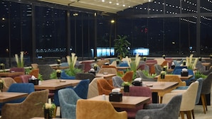 A modern restaurant with multiple tables and chairs, large windows, and indoor plants. - Grand Rimedya Hotel Bursa (Bursa)
