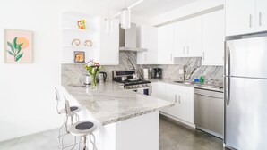 Une cuisine moderne avec des meubles blancs, un plan de travail en marbre, des appareils électroménagers en acier inoxydable et un coin bar avec des tabourets.