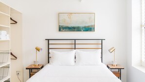 Une chambre bien rangée, avec un lit, deux tables de chevet, une lampe fixée au mur et une étagère avec des serviettes.