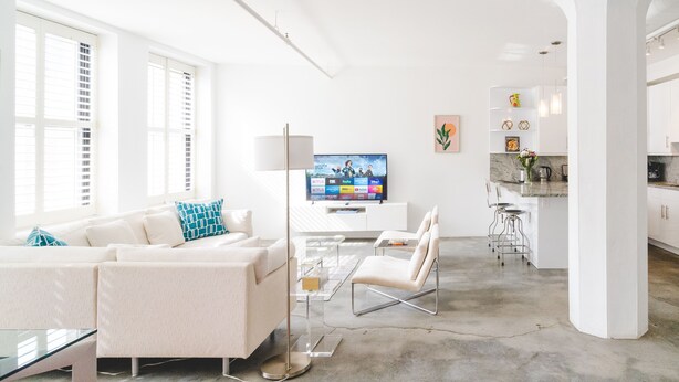 Un salon moderne avec un canapé, un téléviseur et une table basse en verre. Il y a également un coin cuisine avec un bar et une table à manger.