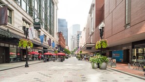 Une rue de la ville bordée de boutiques, avec des terrasses et des jardinières suspendues remplies de fleurs.