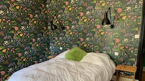 Een slaapkamer met bloemenbehang, een wit bed en een groen kussen.