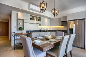 A modern kitchen with a dining table set for four, equipped with a built-in oven, microwave, and stainless steel refrigerator. - Luxury Ocean View Condo | Pools, Hot Tubs, Gym, BBQ, Walk To The Beach (Puerto Vallarta)