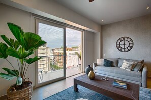 A modern living room with a large window, a sofa, a coffee table, and a potted plant.