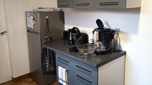 A compact kitchen with grey cabinets, a refrigerator, a coffee maker, and a kettle on the countertop.