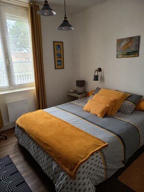 A bedroom with a bed, a bedside table, a lamp, a picture frame, and a window with curtains. - House near sea 7 sleeps (Pornic)